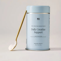 Daily Creatine Support tin with a scoop of powder on a gold spoon.