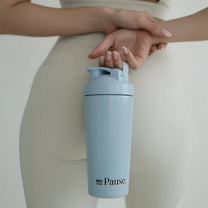 A woman in cream activewear holding the MyPause steel shaker bottle.